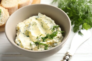 Fototapeta premium Delicious butter with herbs in bowl, bread and knife on white wooden table, closeup