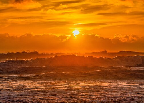 Beautiful golden sunset above powerful ocean waves with dramatic clouds and warm orange light. Atmospheric tropical seascape background with dynamic surf and glowing horizon