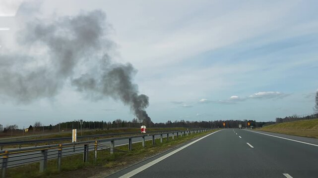 Dark Smoke Rising Beside Empty Highway, dramatic travel video frame with forest fire plume near road under cloudy sky