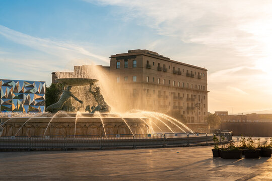Landscape shot looking past triton fountain landmark in valletta main gate plaza at sunset golden hour with Clear blue skies overhead and buildings in the background with limestone material