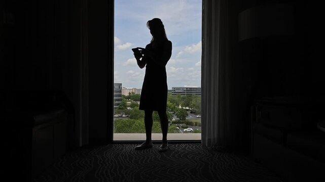 Woman working phone in room silhouette.