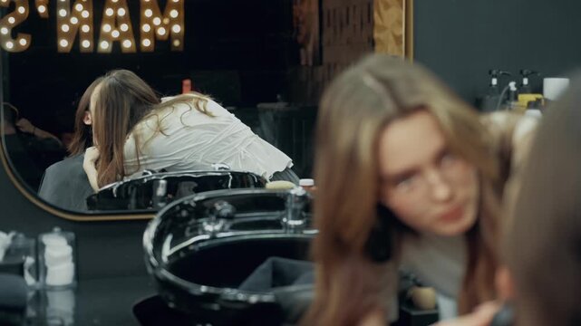 Professional female barber trimming beard of male client with electric clipper during grooming procedure in modern barbershop