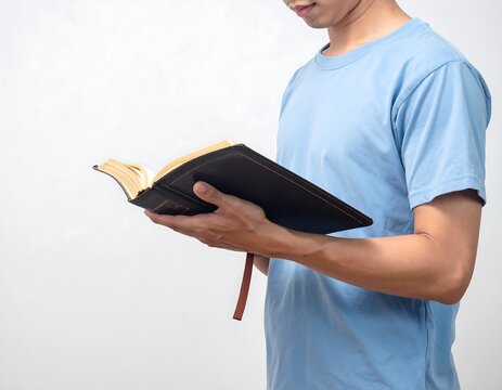 A person in a light blue shirt holds an open, hard-covered book with a golden-edged pages and bookmark, against a white backdrop