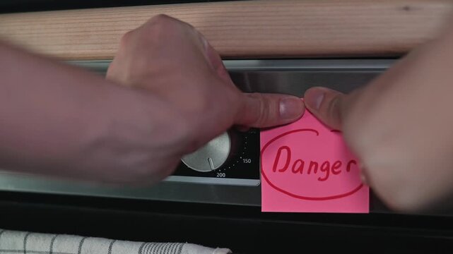 A hand reaches to place a sticker labeled Danger on an oven dial. This act signifies a caution about possible risks associated with high-temperature cooking
