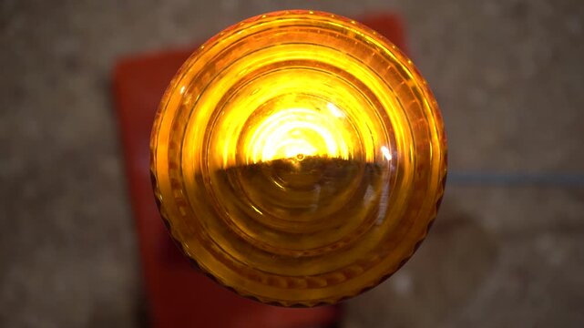 Top-down extreme close-up of a rotating amber hazard warning light. The pulsating yellow-orange glow is perfect for illustrating caution, road safety, construction, and emergency alerts.