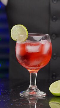 Cold alcoholic drink and male hand accurate holding dry slice of orange or lime lemon with tweezers over it at establishment.