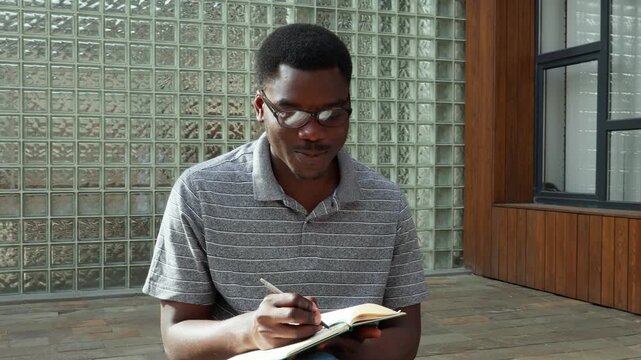 Student writes notes at a study spot by a glass brick wall in summer