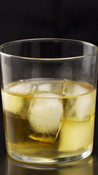 Professional bartender serving a cocktail in the glass with one big ice cube on the bar counter in the blurred