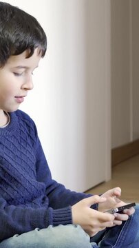 Lonely child with his phone. A little boy playing with a smartphone at home.
