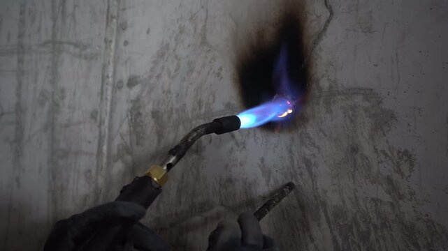 Close-up of a worker using a blowtorch to heat a concrete wall penetration for chemical anchoring or waterproofing. Includes authentic roaring audio. Essential B-roll for civil engineering projects.