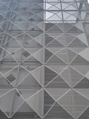 Obraz premium Close-up of a perforated metal wall with a triangular pattern on a modern building. Ideal for corporate presentations, representing transparency, structural integrity, and modern design.