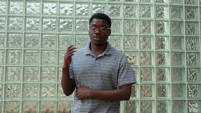 Man performs a sign language interpretation in front of a glass block wall while interacting and expressing ideas clearly