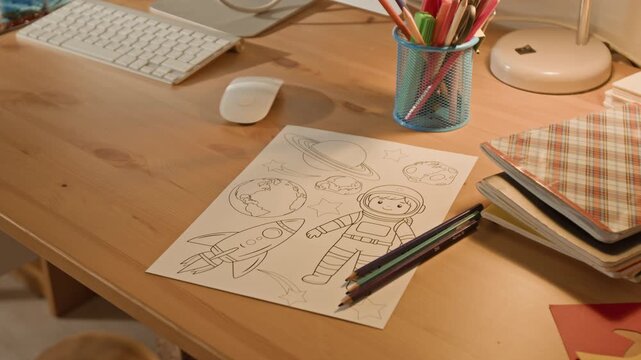 No people close-up of child drawing and color pencils, representing astronaut, space rockets, planets, on desk next to computer keyboard and mouse, suggesting fun creative break during homework