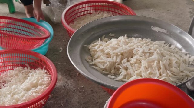 The process of preparation of ingredients for Maphrao Kaew (crystallized coconut strips) or a similar coconut-based dessert in Vietnam. Coconut chunks are placed in plastic baskets
