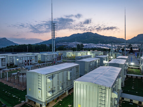 Large-scale containerized battery energy storage system at dusk in an outdoor industrial facility with mountainous background