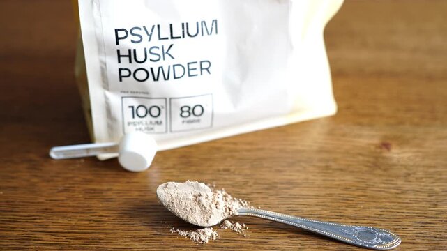 Psyllium husk powder on a spoon on a wooden table next to the packaging.