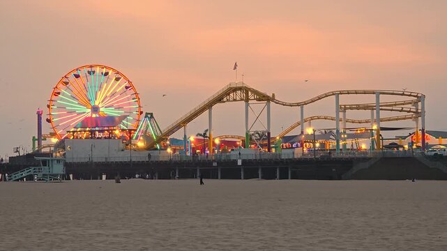 Santa Monica Pier At Sunset With Ferris Wheel Lights, cinematic coastal video frame with amusement rides and warm sky