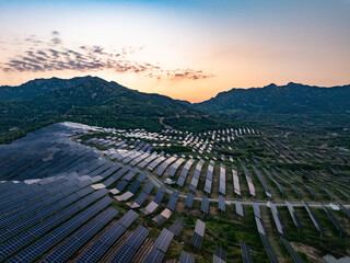 Fototapeta premium Aerial view of mountainous photovoltaic power station during sunset with solar panels arranged in rows across hills