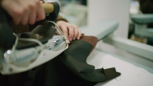 Close up of a tailor using a professional steam iron on black fabric in a fashion workshop