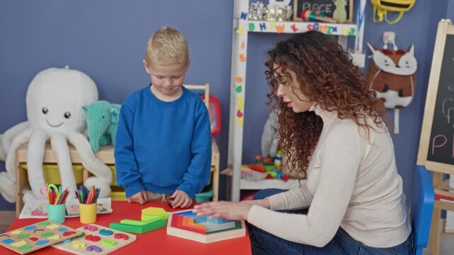 Woman teacher arranging wooden stacking blocks with hands while little boy watches in a classroom; focused learning.