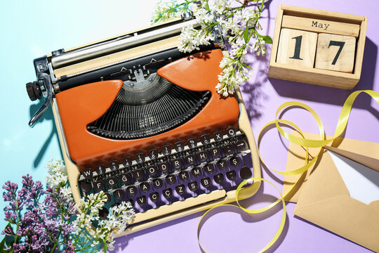 Vintage typewriter, envelopes, ribbon, block calendar and lilac flowers on color background, flat lay