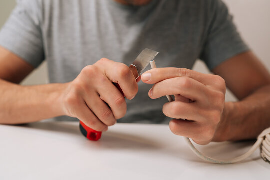 Close-up of electrician hands splitting communication cable with utility knife sitting at white table, preparing data wires for connection and installation, performing electrical repair work.