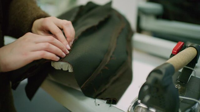 Close up of a tailor using a professional steam iron on black fabric in a fashion workshop