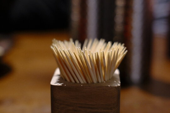 Many light colored toothpicks stand upright in a dark wooden holder on a table indoors.