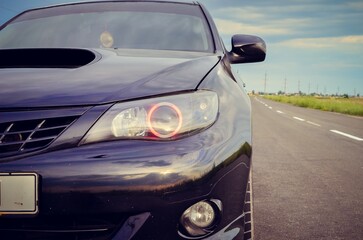 Naklejka premium A close front detail of a sporty car with a dramatic headlight design in a scenic outdoor location. This image combines automotive style, performance, and lifestyle appeal, perfect for advertising.