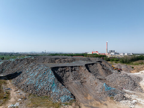 Industrial waste slag dump site with distant power plant chimney under clear sky