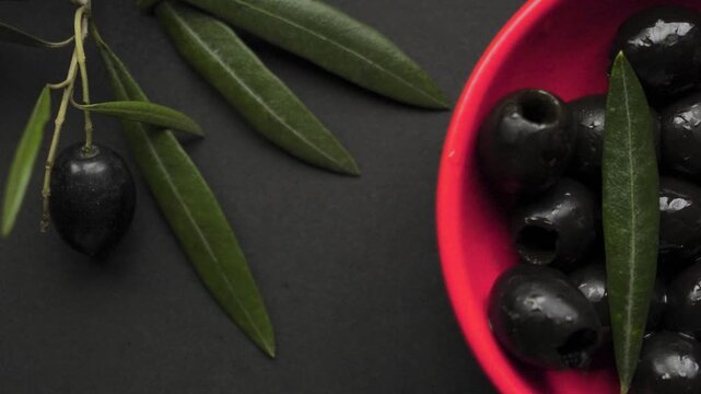Red bowl with black olives enters frame against black background
