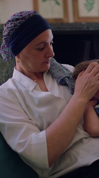 Mother with headscarf gently caressing toddler hair at home, chemotherapy recovery and cancer journey, tenderness and emotional caregiving in quiet intimate family moment