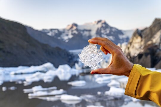 Hand holding glacial ice, Sv&iacute;nafellsj&ouml;kull glacier, Hvannadalshn&uacute;kur mountain behind, Vatnaj&ouml;kull National Park, Skaftafell, South Iceland, Iceland