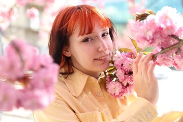 Naklejka premium Beautiful young girl posing near blossoming sakura tree outdoors