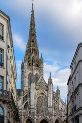 Fototapeta premium View of Rouen Cathedral in France rising between tall urban facades, highlighting contrast of medieval stone details and surrounding European cityscape