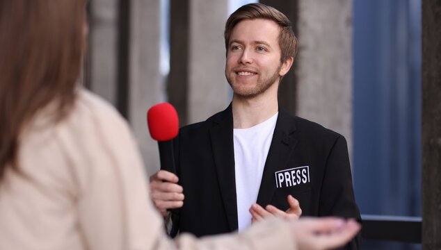 Professional journalist with microphone interviewing woman outdoors