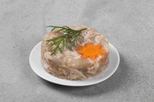 Pork aspic. With carrot flower. On a plate. Light gray background