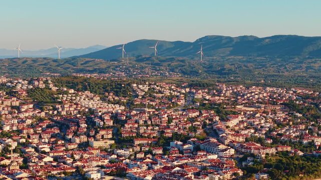 Aerial view of residential town spreading across foothills toward wind turbines , marina of Datcha Turkey.