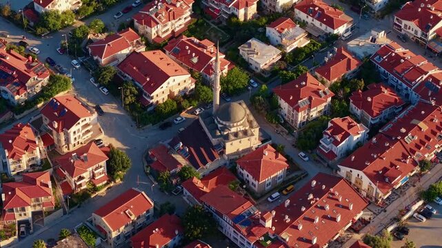 Aerial tracking shot of red roof neighborhood with mosque sweeping over suburban streets at golden hour, Datcha Turkey.