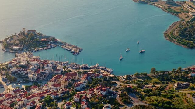Aerial panning shot of coastal town marina with sailboats in turquoise bay and sunlit harbor of Datcha Turkey.