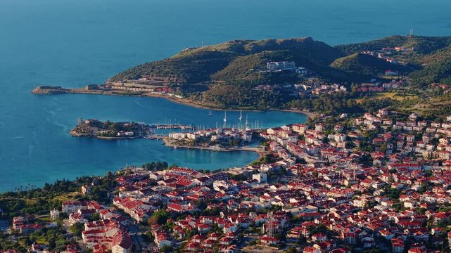 Aerial view of coastal town Datcha Turkey spreading along curved bay with red roofs and marina at golden hour.