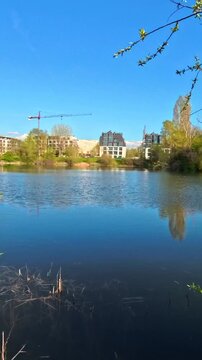 Urban Lake in Early Spring Seen Through Blooming Trees on Shore, Scenic City Park Landscape With Flowering Branches and Water Reflection, Peaceful Nature View in Sunny Weather, Fresh Springtime