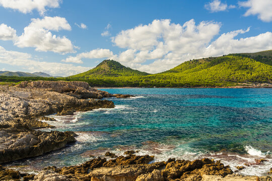 Sunlit transparent sea water splashing over coastal rocks at Cala Agulla beach in Mallorca, Spain. Peaceful Mediterranean seascape and tranquil summer atmosphere