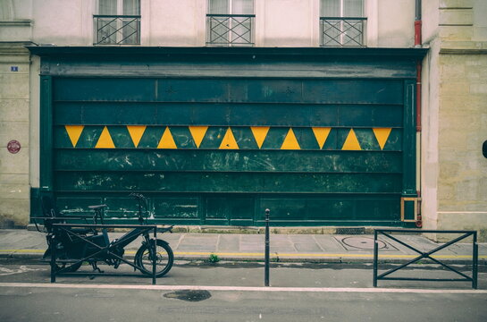 Streets of Paris, France. A black electric bicycle with a rack for two children stands against a green gate.