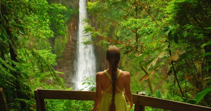 Tourist woman admiring tall Costa Rica waterfall Catarata del Toro from wooden viewpoint in forest