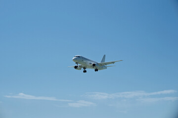 Fototapeta premium White aircraft on final approach against a blue sky with light clouds
