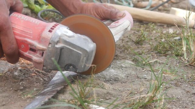 Workers are sharpening or cutting saw blades using a hand grinder in an open area.