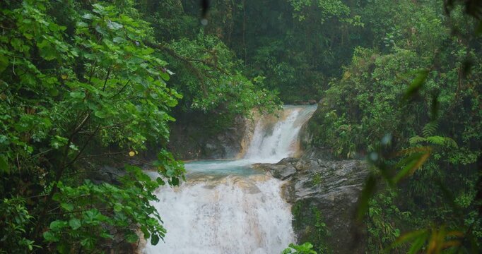 Cascading waterfall surrounded by vibrant green rainforest during rainy weather in Costa Rica