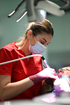 Female Dentist Performing Dental Treatment On Patient In Modern Clinic With Masked Hygienist