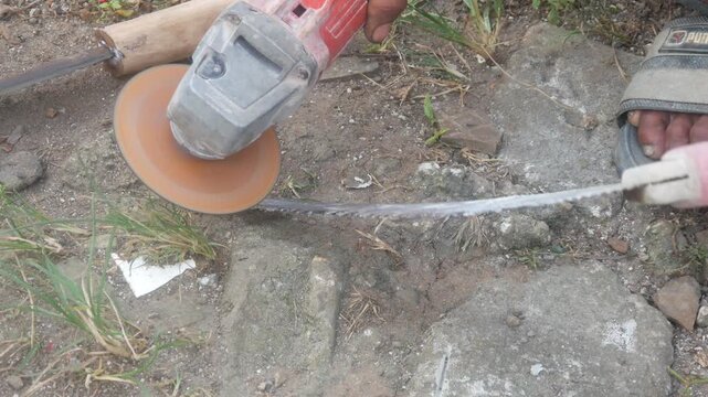 Workers are sharpening or cutting saw blades using a hand grinder in an open area.